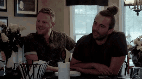 two men are sitting at a table with a basket of paper towels on it