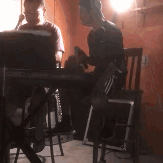 a man is playing a keyboard and another man is sitting in a chair holding a microphone