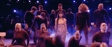 a group of people are dancing on a stage with the word live in the corner