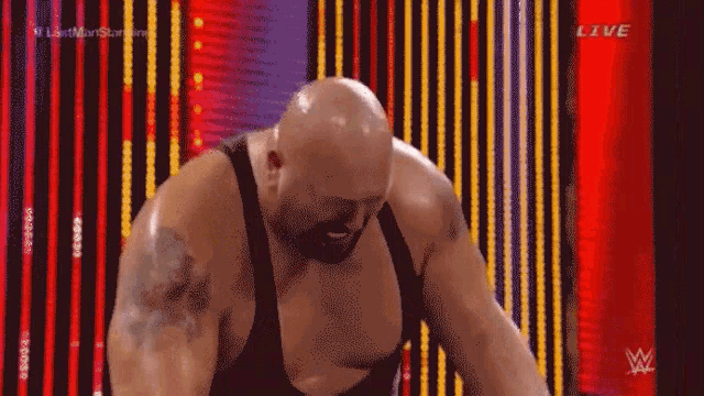 a bald man with a tattoo on his arm stands in front of a red wall with the words live on it