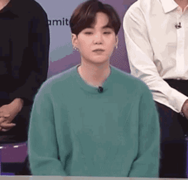 a young man in a green sweater is sitting in front of a microphone .