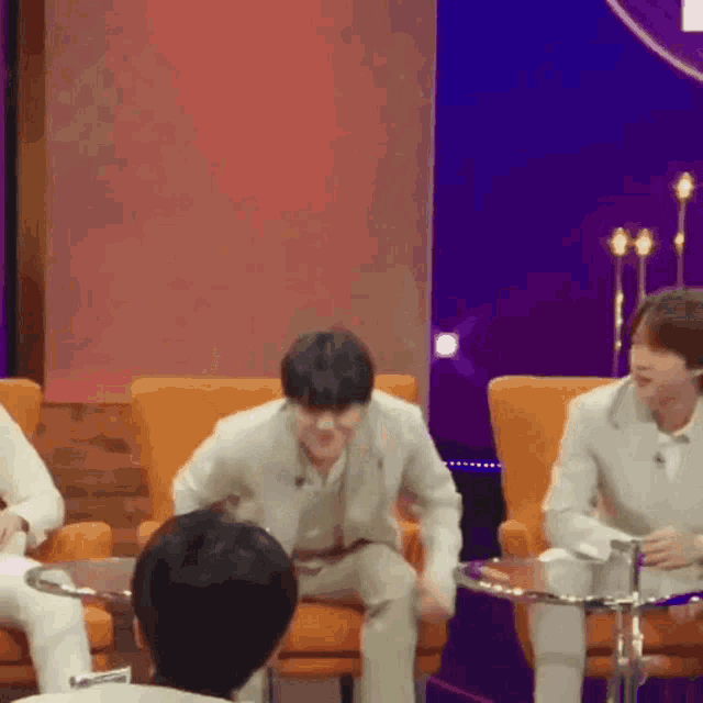 a group of men are sitting in chairs on a stage and one of them is laughing .