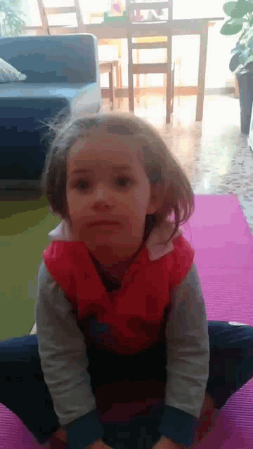 a little girl is sitting on a pink mat and making a face