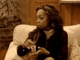 a woman is sitting on a couch smoking a cigarette and drinking from a glass .