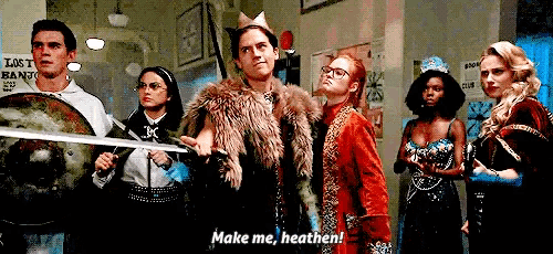 a group of people are standing in a room and one of them is holding a sword and saying " make me heathen "