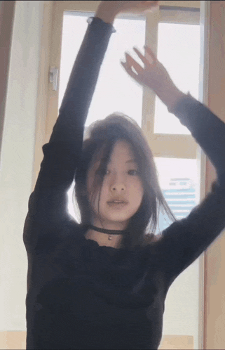 a woman in a black shirt is standing in front of a window with her hands in the air