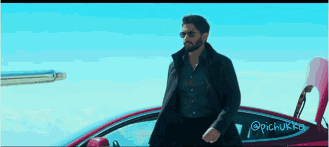 a man wearing sunglasses is standing next to a red car with the hood open