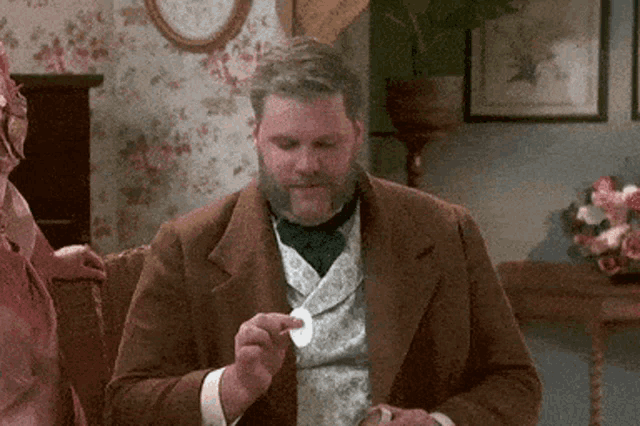 a man with a beard is sitting on a couch and holding a piece of paper in his hand .