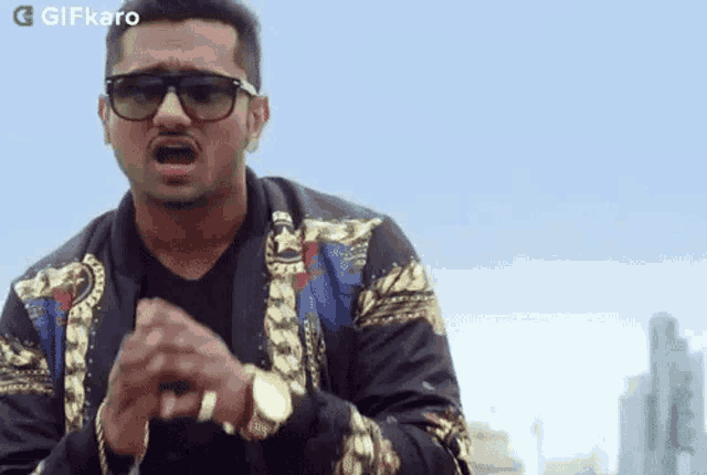 a man wearing sunglasses and a gold watch is standing in front of a city skyline .