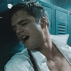 a man without a shirt is sitting in a locker room with his mouth open .