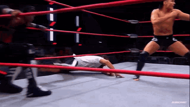 a man is laying on the ground in a wrestling ring while another man is standing in the ring .