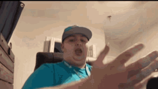 a man in a blue shirt and hat is sitting in a chair with his hands outstretched in a room .