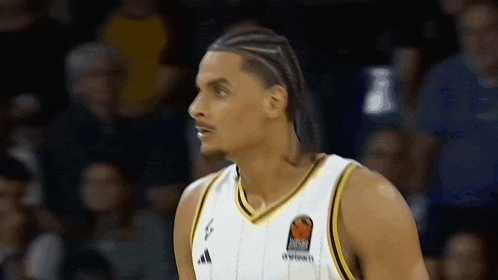 a basketball player wearing a white and gold jersey is looking at the camera .