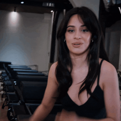 a woman in a black tank top is standing in front of a row of exercise machines