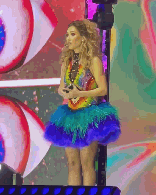 a woman in a rainbow dress is standing in front of a large eye
