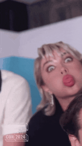 a woman is making a funny face in front of a sign that says ' con 2024 '