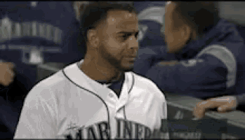 a man in a mariners jersey is standing in the dugout .