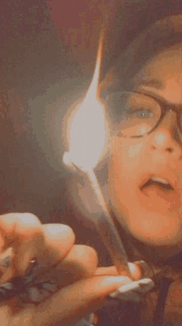 a woman wearing glasses is lighting a cigarette with a match