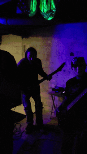 a man playing a guitar in a dark room with purple lights behind him