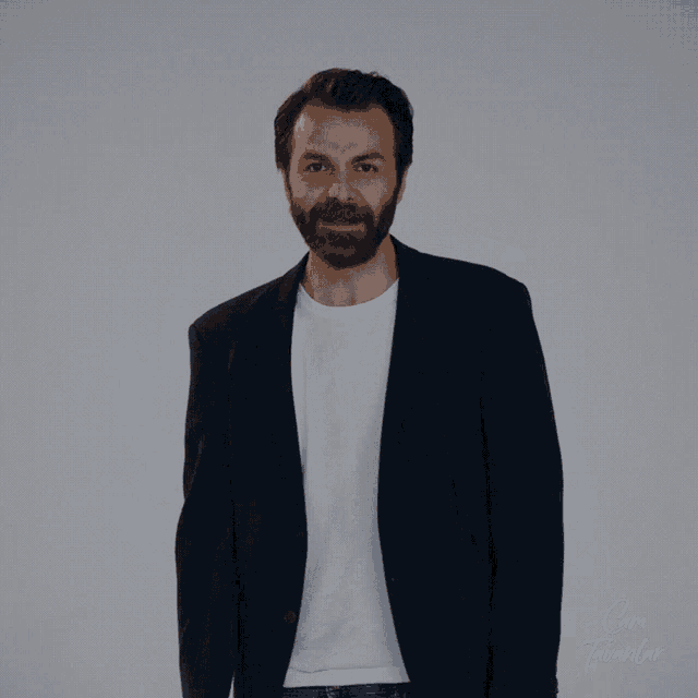 a man with a beard is pointing at the camera with a white shirt underneath him that says ' cem '