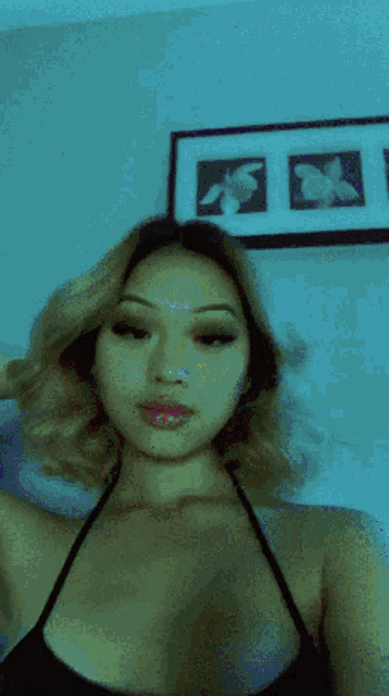 a woman in a black top is taking a selfie in front of a framed picture of flowers on the wall .