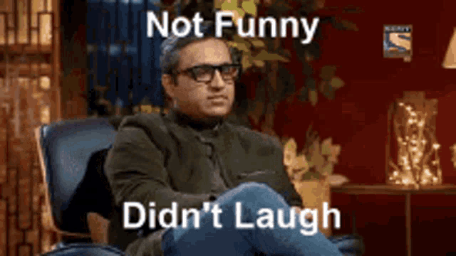 a man wearing glasses is sitting in a chair with the words not funny didn 't laugh written above him .