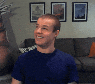 a man wearing a blue shirt is smiling in front of a couch