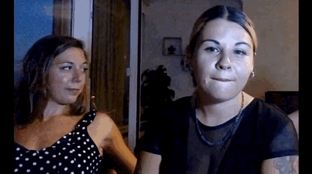 two women are standing next to each other in a room and looking at the camera .