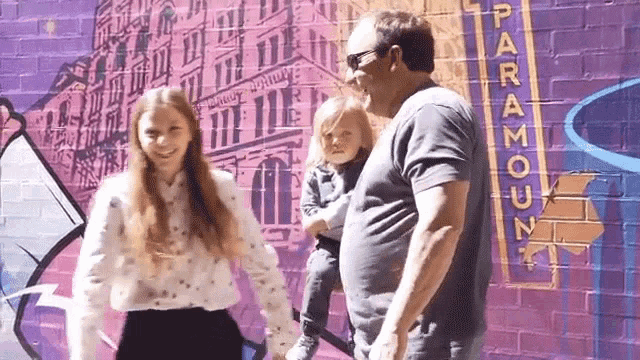 a man and two children are standing in front of a mural on a brick wall .