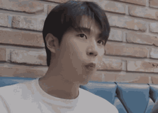 a young man is sitting on a blue couch in front of a brick wall making a funny face .