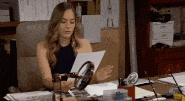 a woman sits at a desk looking at a piece of paper with the word ope written on it