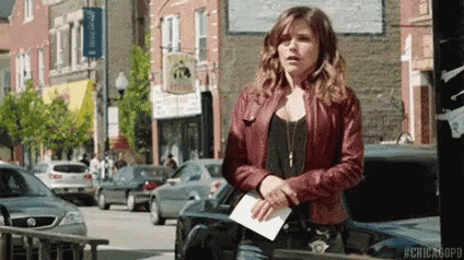 a woman in a red leather jacket is standing on a city street with a piece of paper in her hand .