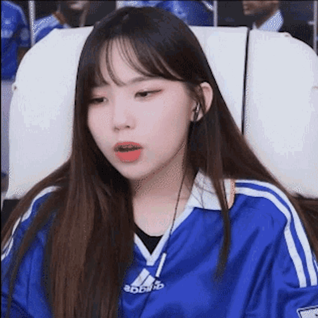 a young woman wearing a blue adidas shirt is sitting in a chair with her mouth open .