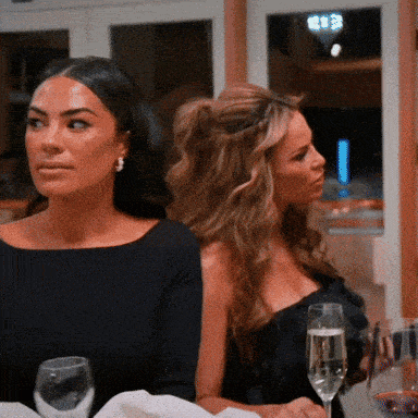 two women are sitting at a table with a glass of wine