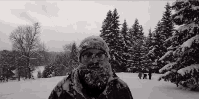 a man with a beard and glasses is standing in the snow with trees in the background