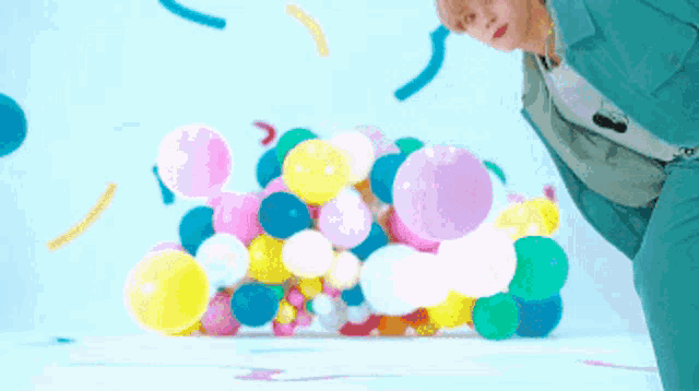 a man in a green suit is standing in front of a pile of balloons .
