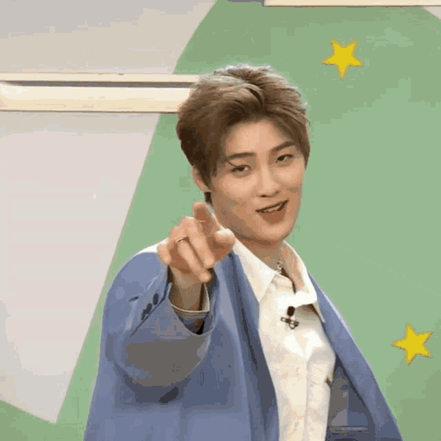 a young man in a blue jacket and white shirt is pointing at the camera .
