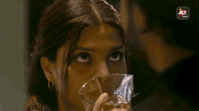 a close up of a woman drinking from a glass with a alt logo in the background