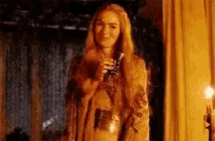 a woman in a gold dress is holding a glass of wine in her hand .