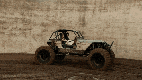 a jeep is driving through a muddy area with a wall behind it
