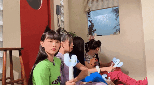 a group of young girls are sitting in a room holding fans
