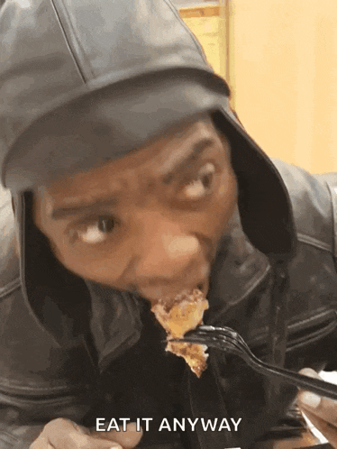 a man in a leather jacket is eating a piece of food with a fork and the words eat it anyway above him