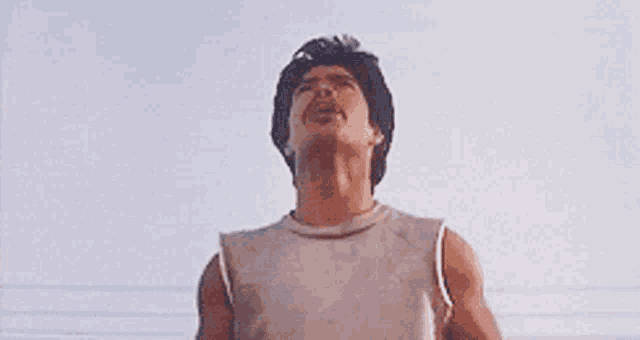 a man in a white tank top is looking up at the sky .