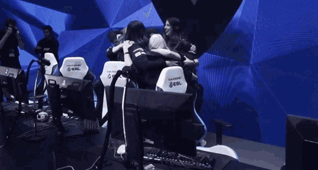 a group of people hugging in a room with gaming chairs that say esl on them