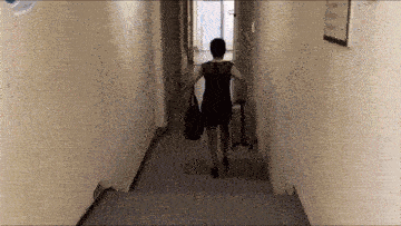 a woman in a black dress is walking down a hallway carrying a bag .