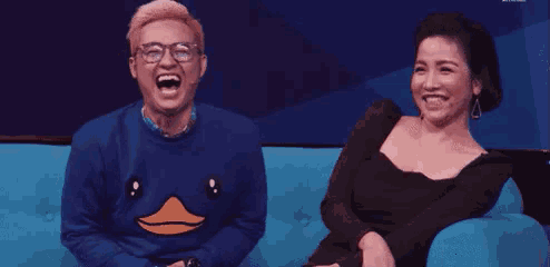 a man and a woman are sitting on a blue couch and laughing .