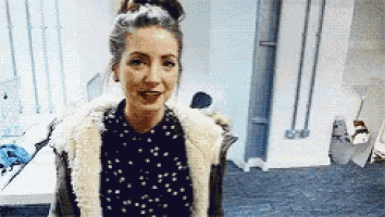 a woman is standing in a room wearing a fur coat and a polka dot shirt .
