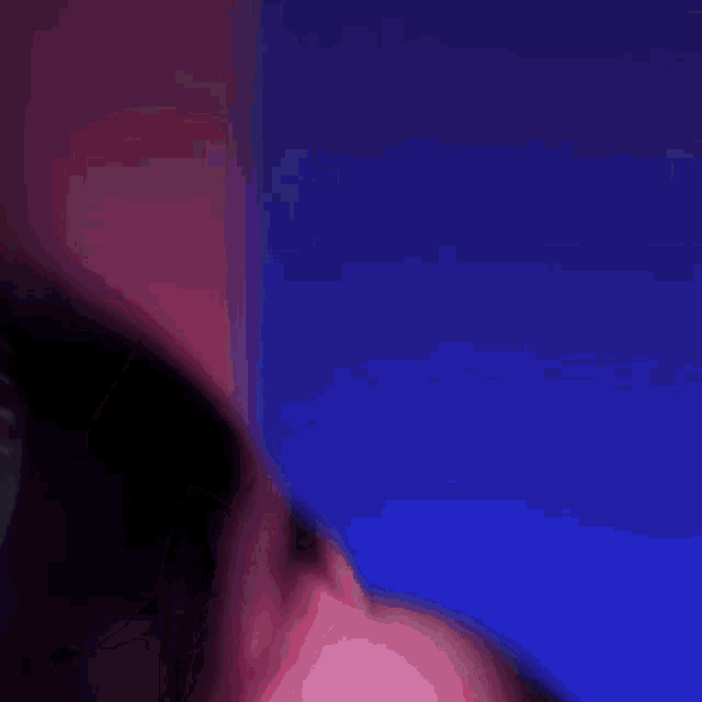 a woman in a pink hoodie is standing in front of a blue wall with her hair blowing in the wind .