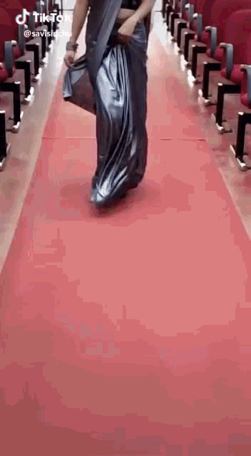a woman in a saree is walking down a red carpet in an auditorium .