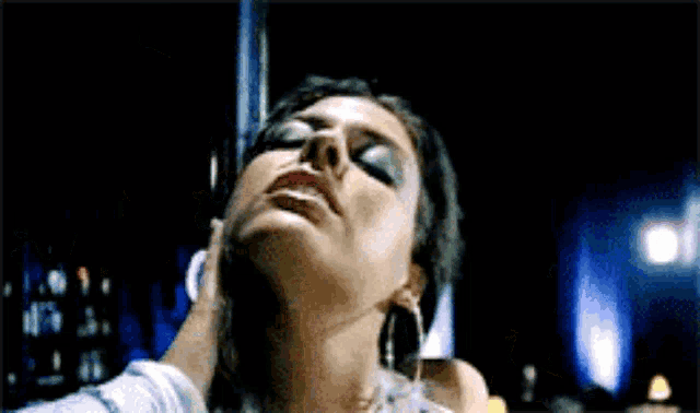 a woman is laying on a pole in a dark room and a man is touching her neck .